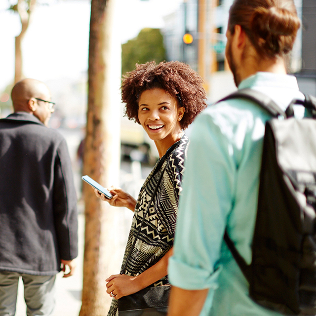 Woman smiling at a person behind her while holding a mobile phone