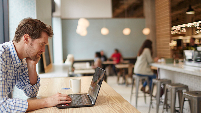 A man sitting in a coffee shop and browsing on his laptop.